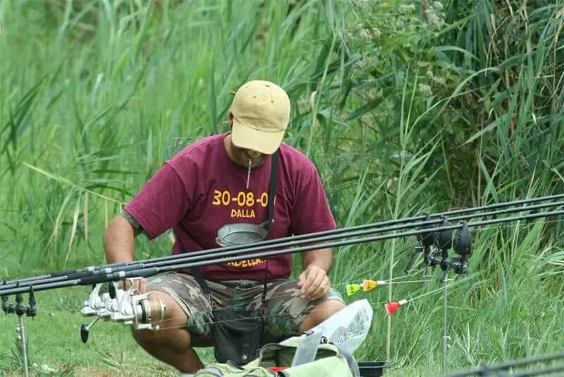 Man Cleaning Fishing Rod While Crouching On Field